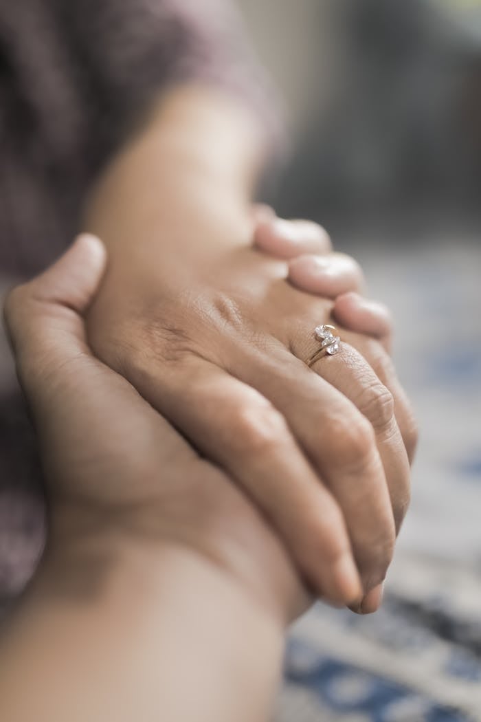Crop unrecognizable tender person holding hand of anonymous married female with precious ring on finger against blurred background on street